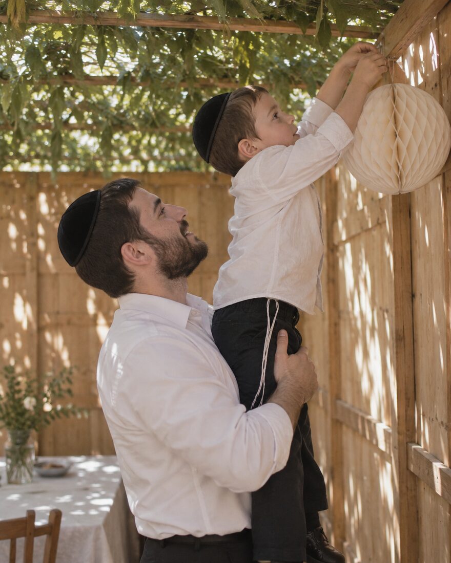 Father lifting son to decorate the sukkah