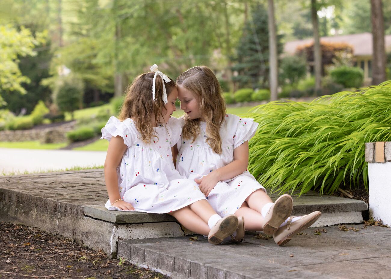 Two sisters in white dresses sitting on garden steps