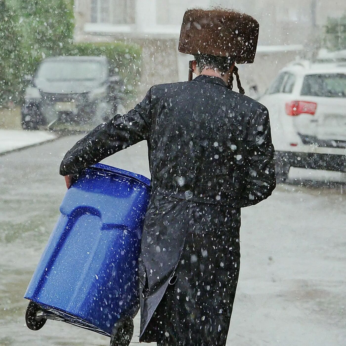 A man pulling a blue recycling bin through the snow